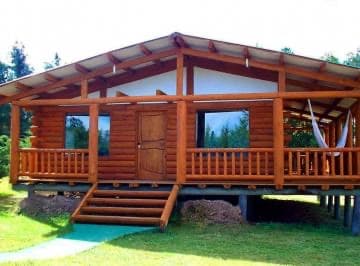 Cabaña de madera con galería y techo a dos aguas, sobre pilotes