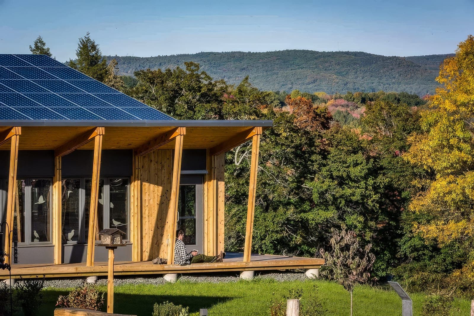 Vivienda de madera con cubierta de paneles solares frente al bosque en otoño